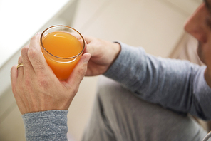 Close-up of man sitting and holding in his hands the glass with orange juice