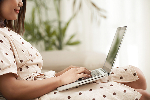 Cropped image of smiling young woman enjoying working on computer when resting on sofa