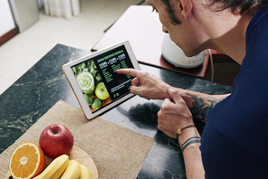 Close-up of man reading a recipe of fruit smoothie on digital tablet and is going to prepare it in the kitchen