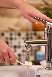 Close-up of woman holding toothbrush with toothpaste under the stream of water and she is going to brush her teeth in the bathroom