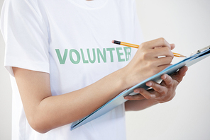Close-up of female volunteer in white t-shirt holding clipboard and making notes with pencil
