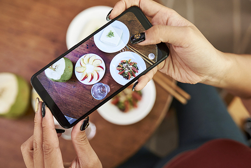 Hands on woman taking photo of dishes on cafe tablet to make a post