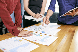 Close-up of business team standing together near the table with documents analyzing business graphs and charts and discussing it