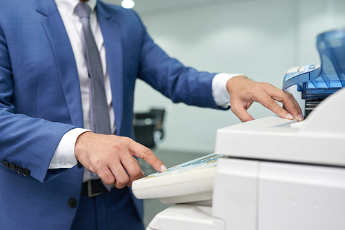 Close-up of businessman in suit standing near the copy machine and making a copy of document at office