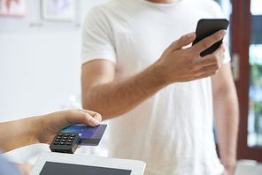 Close-up of man standing with mobile phone while woman making payment by credit card on tablet pc