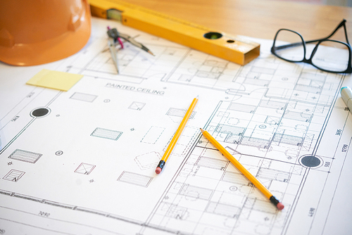 Two pencils lying on construction plan near glasses and hardhat on office desk