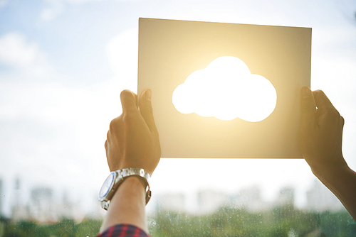 Crop hands holding paper sheet with cut shape of cloud and holding against window with bright sunlight behind
