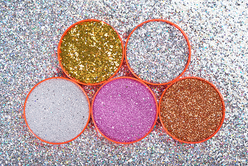 From above shot of bright glitters of different colors arranged in lids on silver glowing surface