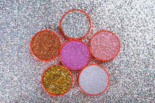 Top view of composed circle lids filled with various bright glitters and arranged on silver shiny surface