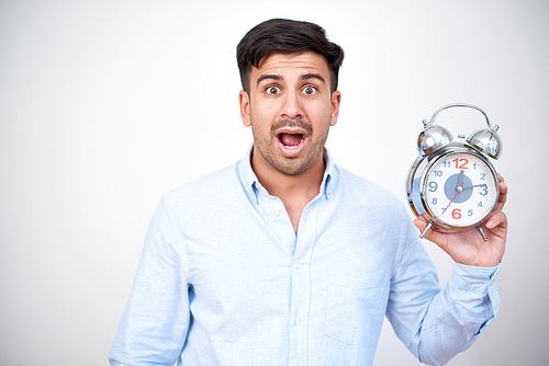 Surprised young man holding and showing time on his alarm clock he fears being late