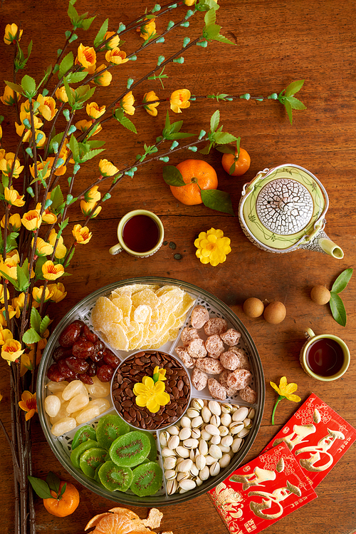 Plate with dried fruits and nuts, apricot branches and greeting cards with best wishes on Chinese New Year table