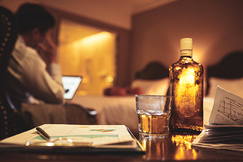 Financial report, whiskey bottle and glass on table in hotel room of businessman