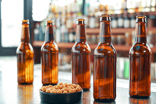 Brown glass beer bottles with small bowl of salty nuts arranged on top of counter in modern bar