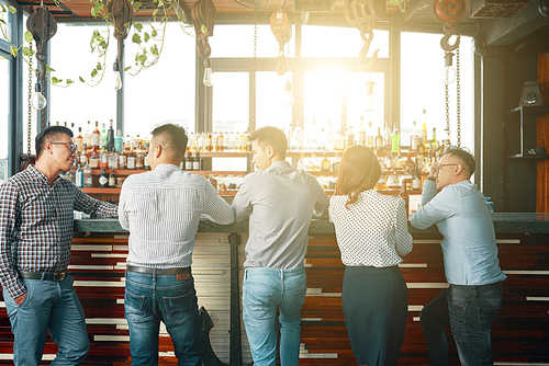 Back view of men and woman gathering at bar counter in bright sunlight having meeting together
