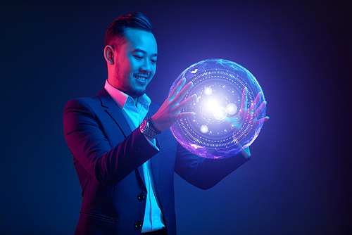 Smiling Vietnamese businessman holding glowing ball with modern interface