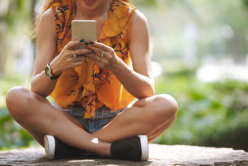 Cropped image of young woman sitting outdoors and texting friends