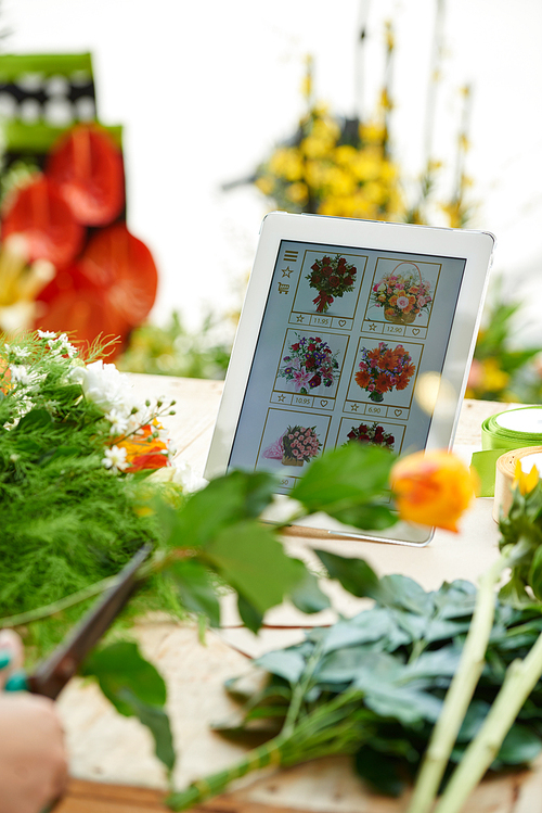 Digital tablet with flower shop application and orders from clients on table of florist