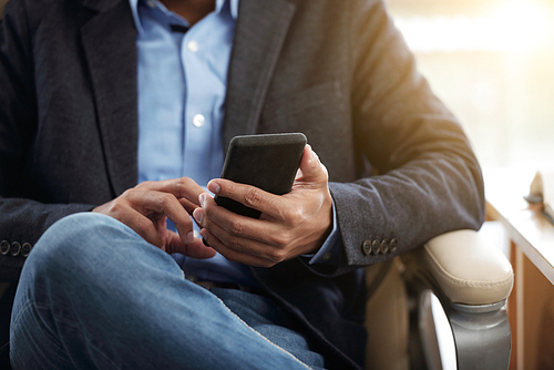 Cropped image of businessman sitting in armchair and reading message in smartphone