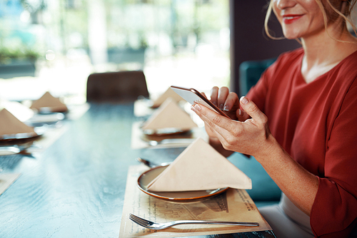 Close-up image of woman sitting at table in restaurant and using smartphone