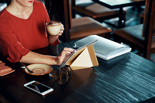 Cropped image of woman drinking latte and using application on digital tablet