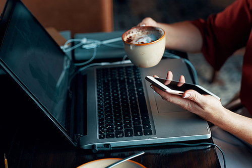 Close-up of woman connecting mobile phone to the laptop and drinking coffee