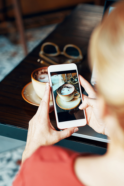 Woman taking photo of coffee cup on smartphone