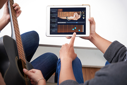 Young people watching acoustic guitar tutorial on digital tablet