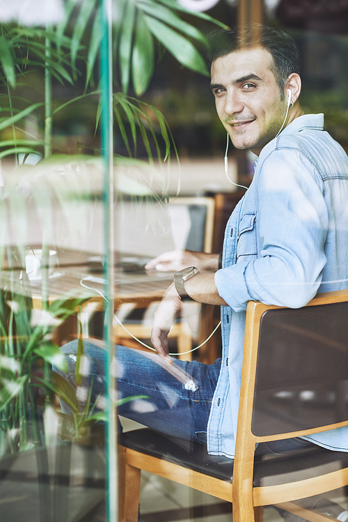 Portrait of handsome young man sitting at cafe table and turning back to camera