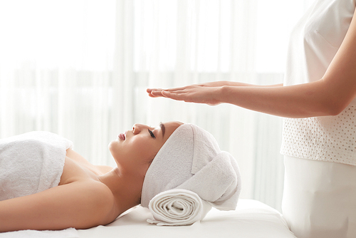 Reiki therapist holding hands over head of pretty female patient