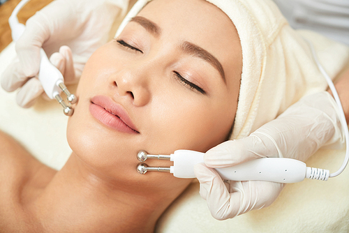 Attractive young woman enjoying microcurrent procedure in spa salon