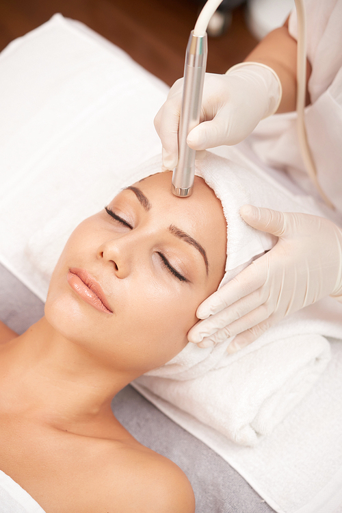 Relaxed woman lying in beauty salon and having anti-wrinkle therapy on her forehead