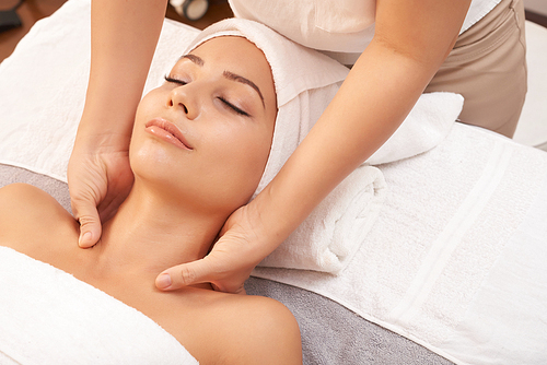 Young female lying on soft towels in spa salon and enjoying relaxing massage of her neck