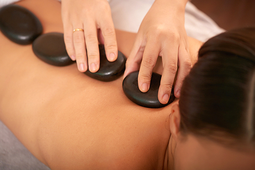 Back of young relaxed female having spa stone massage in modern bodycare salon