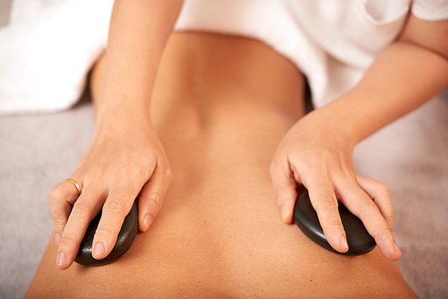 Hands of beautician putting hot spa stones on back of client during beauty procedure