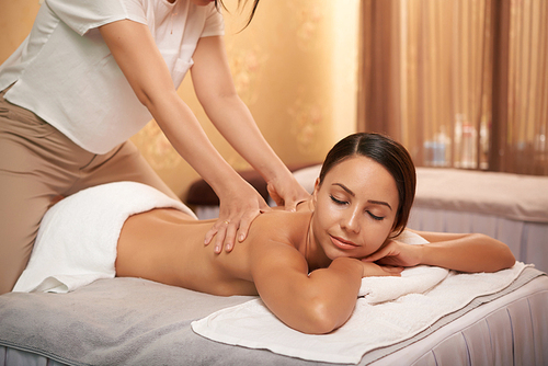 Beautiful young woman enjoying professional back massage in spa salon
