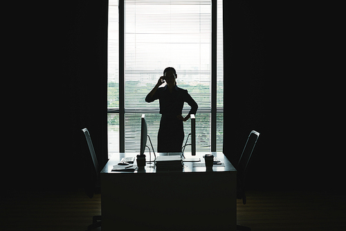 Silhouette of business woman talking on phone against office window