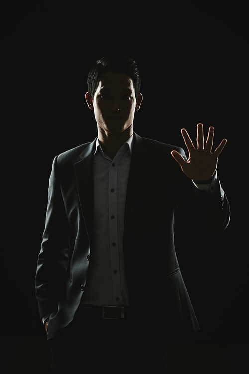 Young Asian businessman showing stop sigh with his hand, photo in dim light