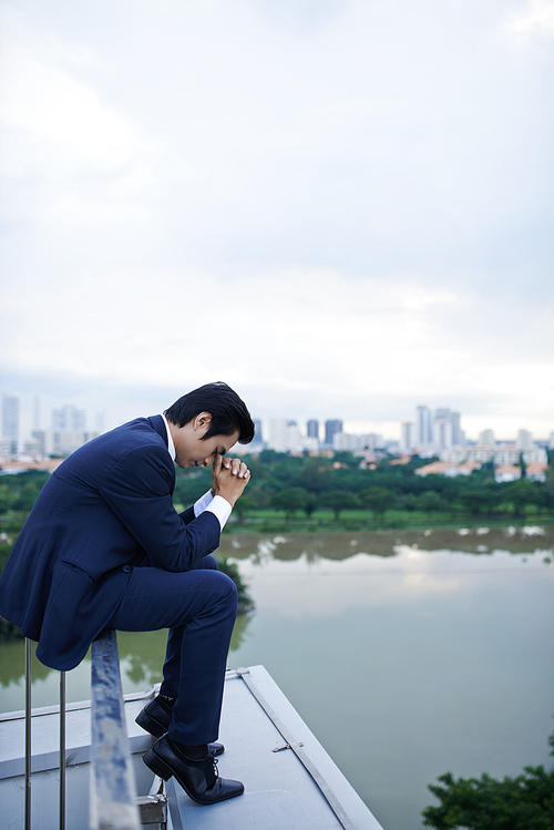 Sad stressed young businessman sitting on rooftop after difficult day