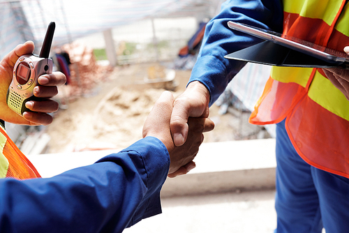 Construction engineers with walkie-talkie and tablet computer shaking hands