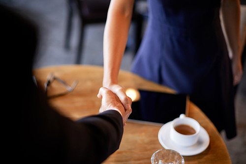 Business executives shaking hands over cafe table to greet each other