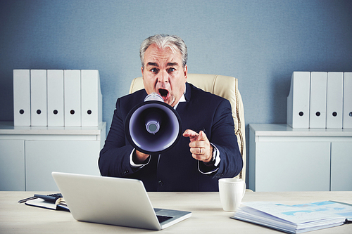 Middle-aged businessman shouting in loudspeaker and pointing at camera