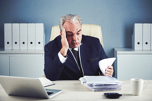 Bored unhappy businessman looking at stack of documents in front of him