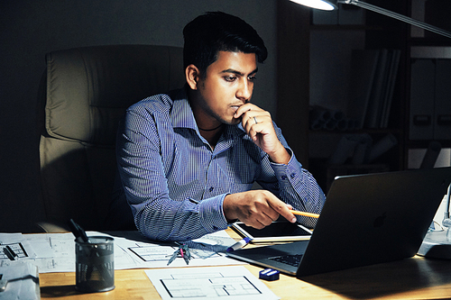 Pensive young engineer working in dark office late at night