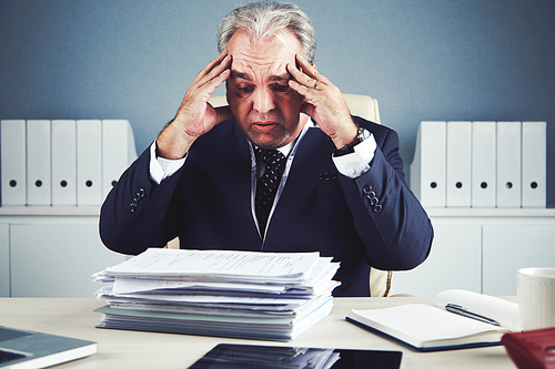 Frustrated businesman in panic looking at stack of documents on his table