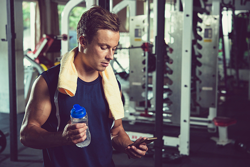 Fit man with water bottle reading message on smartphone