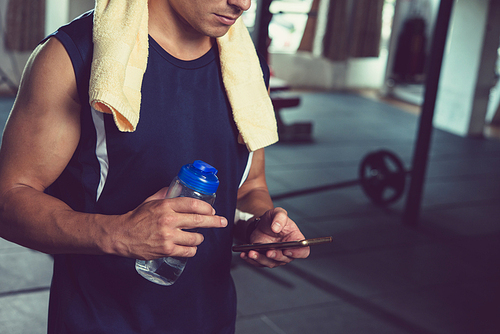 Cropped image of fit man drinking water and using application in his smartphone