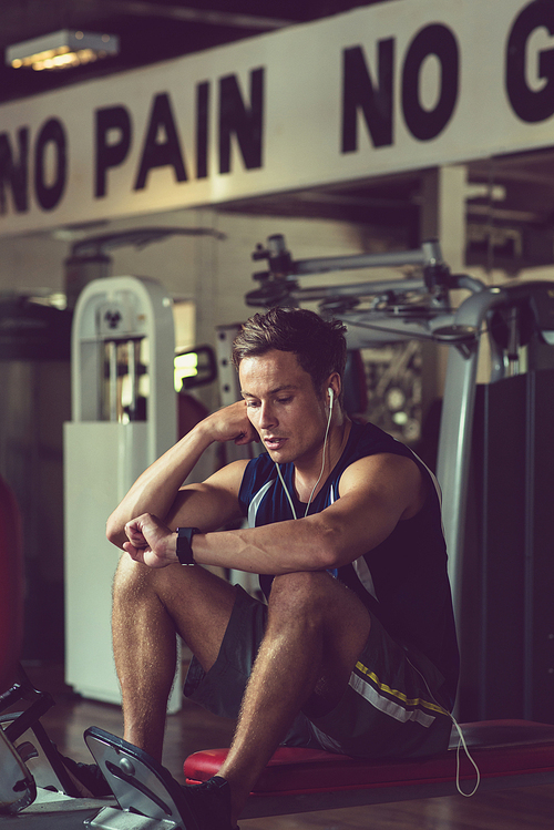 Tired man in earphones checking smart watch after training