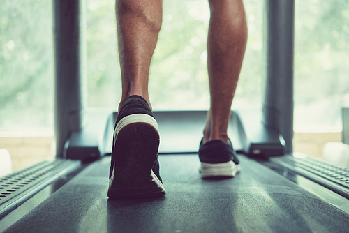 Feet of man walking on threadmill, view from the back