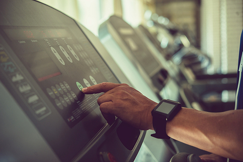 Close-up shot of sporty man adjusting speed on treadmill while having intensive training at modern gym