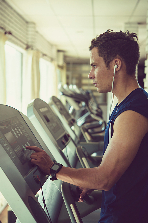 Handsome athlete in earphones setting program on threadmill